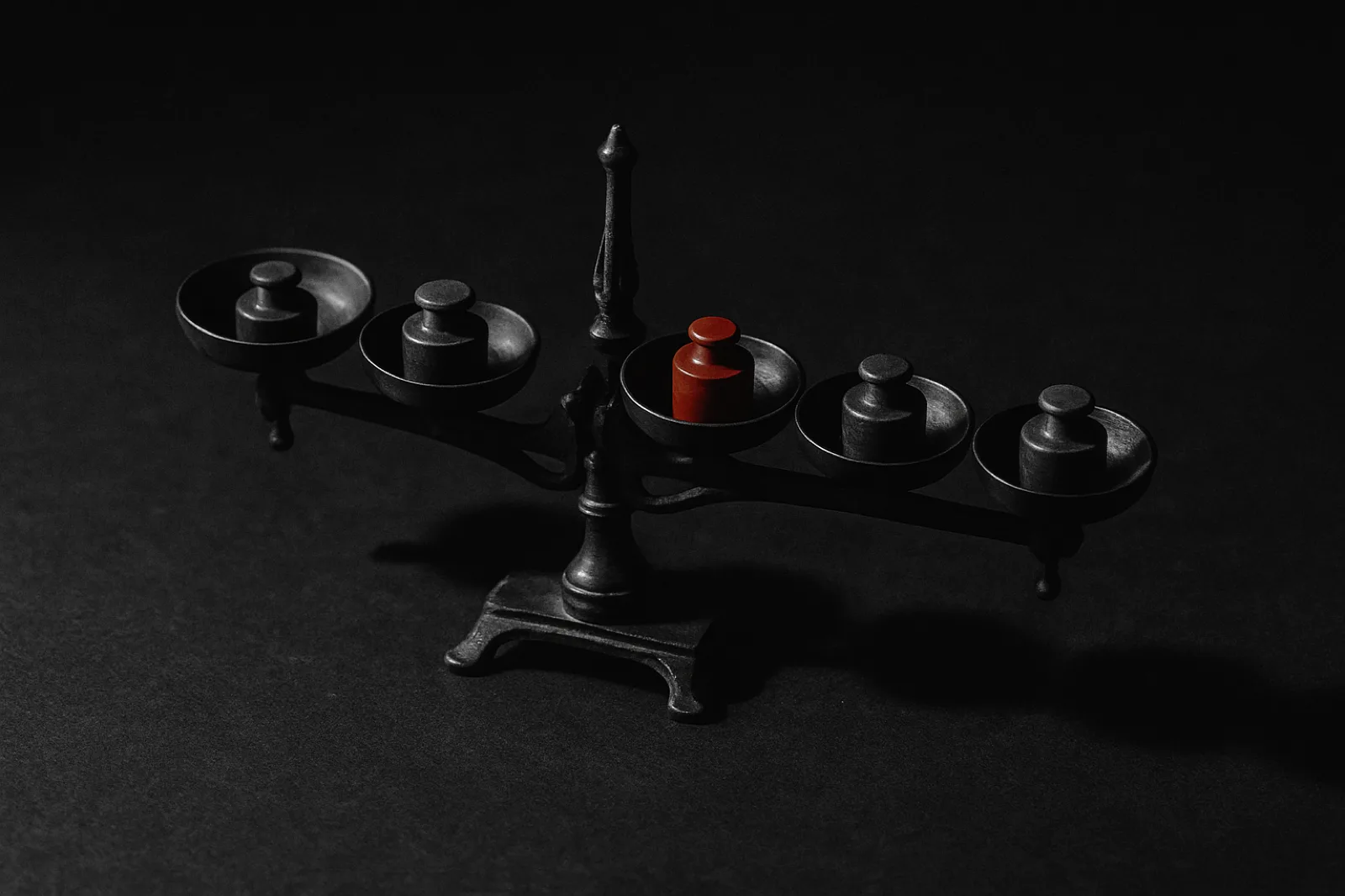 A balance scale with five separate pans, one holding a red weight